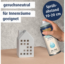 Eine Hand hält eine Sprühdose Belton Aqua Colours matt RAL 7035 zum Bemalen eines kleinen Keramikhauses mit Hinweisen zu Geruchsneutralität