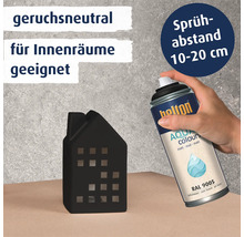Hand hält eine Sprühdose mit Aqua Colours Lackspray in der Farbe Tiefschwarz zum Besprühen einer kleinen Hausfigur aus Keramik