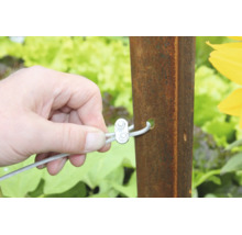 Main fixant un câble métallique avec un serre câble sur un poteau en métal dans le jardin.