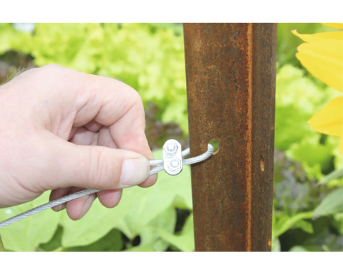 Main fixant un câble métallique avec un serre câble sur un poteau en métal dans le jardin.