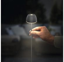 Une main tient une petite lampe de table LED moderne avec un abat-jour nervuré et un pied mince dans un environnement sombre.