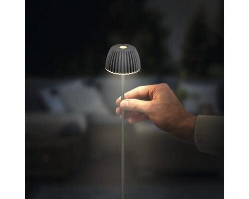 Une main tient une petite lampe de table LED moderne avec un abat-jour nervuré et un pied mince dans un environnement sombre.