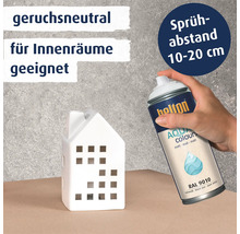 Hand sprüht Belton Aqua Sprühlack auf ein weißes Deko Haus. Informationen zu Geruchsneutralität, Eignung für Innenräume und Sprühabstand.