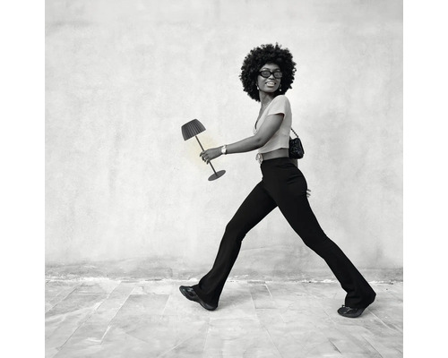Eine Frau mit Afro frisur trägt eine moderne Tischleuchte als Accessoire wie eine Handtasche.