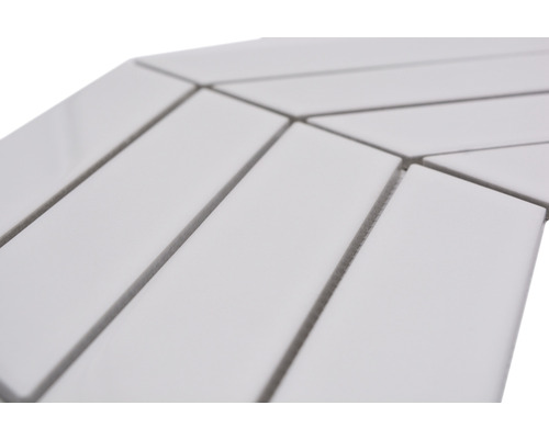 Detailaufnahme von rechteckigen, weißen Keramikfliesen, die in einem Fischgrätenmuster verlegt sind.