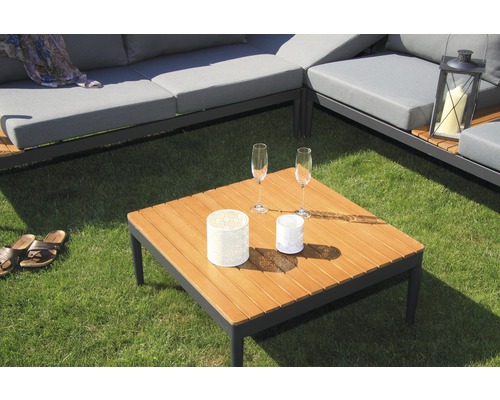 Scène avec mobilier de salon de jardin, composé d''un canapé d''angle avec coussins gris et d''une table carrée en bois avec deux verres et photophores décoratifs