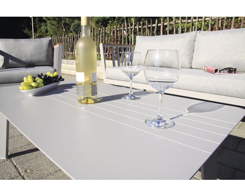 Gartenszene mit Couch, Tisch, Weinflasche und Gläsern für entspannte Stunden im Freien.