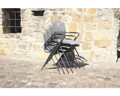 Pile de chaises de jardin avec accoudoirs devant un mur de pierre