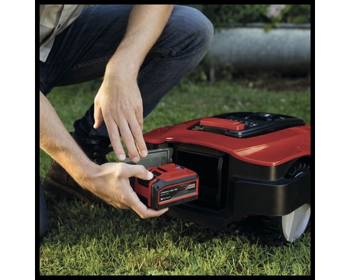 Un homme insère une batterie dans un robot tondeuse.