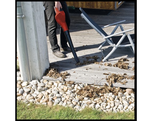 Eine Person benutzt einen Laubsauger, um Laub von einer Holzterrasse zu entfernen.