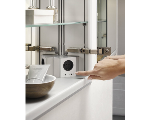 Detailaufnahme eines Spiegelschrankes mit Steckdose und berührender Hand