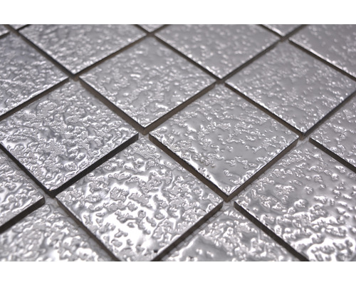 Nahaufnahme von quadratischen, silberfarbenen Mosaikfliesen mit unebener Oberfläche.