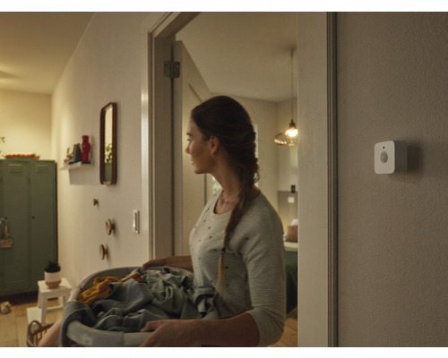 Femme avec un panier à linge dans le couloir avec détecteur de mouvement au mur