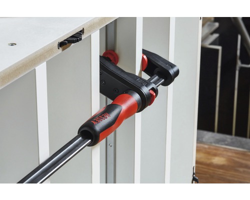 BESSEY Logo. Eine Schraubzwinge fixiert zwei Werkstücke.