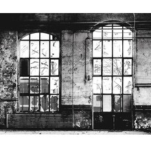 Zwei Fenster in einem alten Gebäude mit beschädigten Scheiben und verfallenden Wänden.