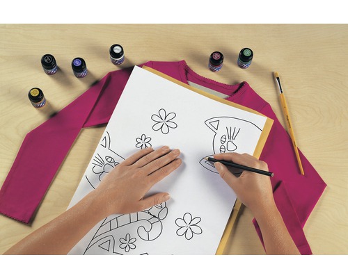 Szene mit einer Person, die ein Katzenmuster mit einem Stift auf ein Blatt Papier zeichnet, zusammen mit Textilfarbe, einem Pinsel und einem T-Shirt.