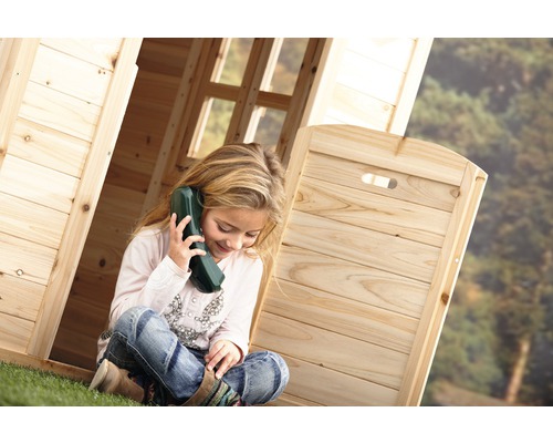 Fille assise avec un téléphone jouet dans une cabane en bois