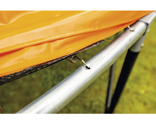 Gros plan d''un ressort de trampoline fixant un coussin de protection de bordure orange au cadre du trampoline.