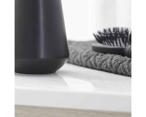 Schwarzer Seifenspender, graues Handtuch und Haarbürste auf einem Waschtisch