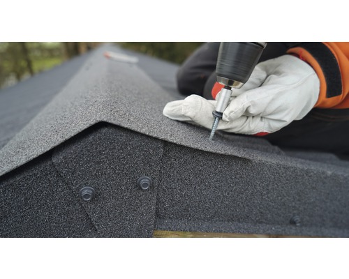 Un artisan fixe des bardeaux bitumés sur un toit avec une visseuse sans fil.