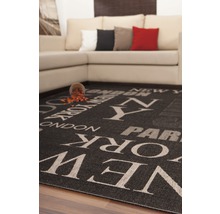 Tapis noir imprimé des noms des villes de New York, Londres et Paris, placé devant un canapé.