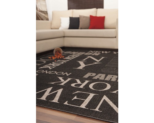 Tapis noir imprimé des noms des villes de New York, Londres et Paris, placé devant un canapé.