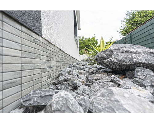 Hauswand mit Sockelverkleidung und Steinen im Garten