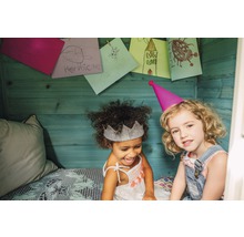 Deux filles avec des chapeaux de fête et des dessins d''enfants sur le mur en bois dans la cabane de jeu.