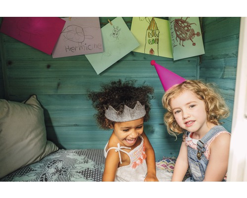 Deux filles avec des chapeaux de fête et des dessins d''enfants sur le mur en bois dans la cabane de jeu.