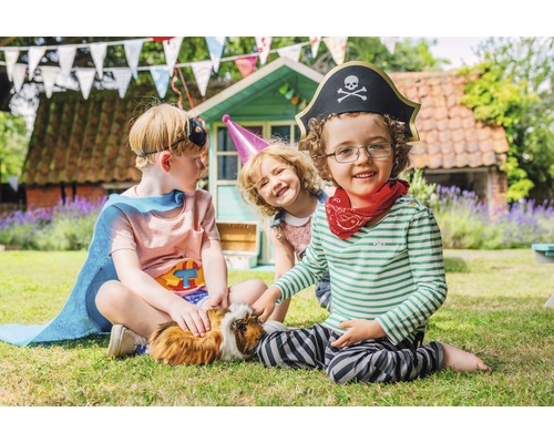 Trois enfants en costumes sont assis avec un cochon d''Inde dans le jardin.