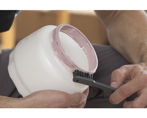 Une personne nettoie un seau de peinture avec une brosse.