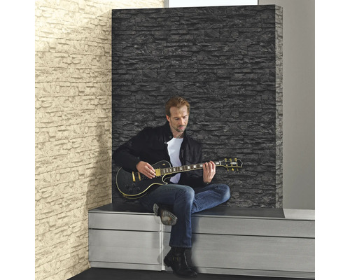 Mann spielt Gitarre vor einer Wand mit Steinoptik Tapete