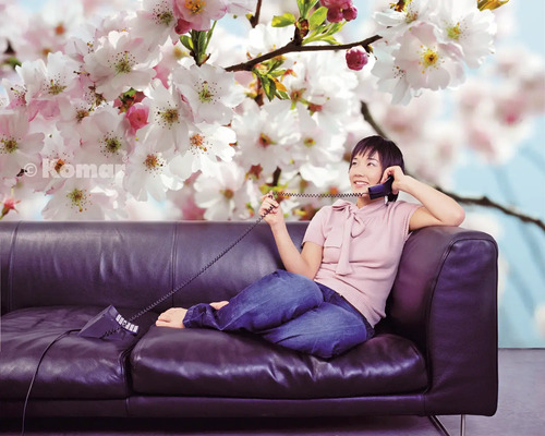 Femme téléphone sur un canapé devant un papier peint photo avec des fleurs de cerisier