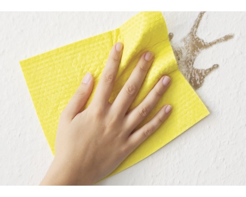 Eine Hand wischt mit einem gelben Reinigungstuch einen Fleck von einer Wand.