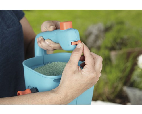 Eine Person bedient einen Streuwagen gefüllt mit Saatgut im Garten.