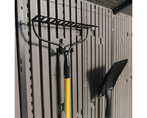 Râteau de jardin avec manche jaune et pelle, fixés à un mur de stockage