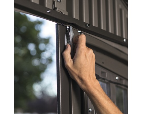 Hand schließt eine Metalltür eines Gartenhauses