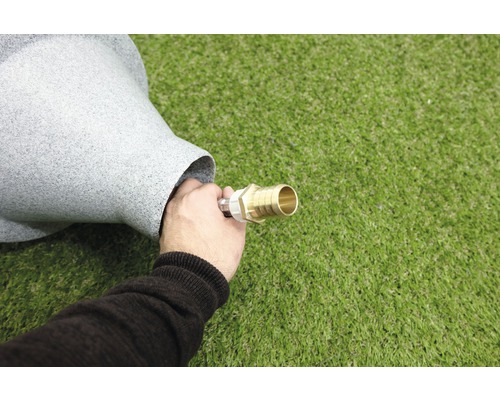 Un homme connecte un tuyau d''arrosage à une fontaine grise.