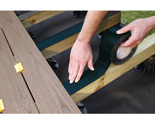 Eine Person befestigt ein Dichtungsband auf einem hölzernen Unterbau für eine Terrasse.