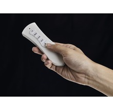 Une main actionne une télécommande blanche pour ventilateur de plafond.