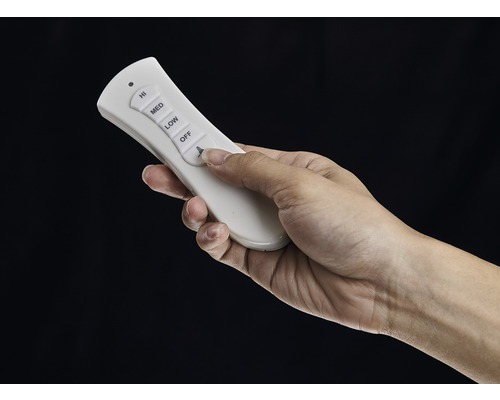 Une main actionne une télécommande blanche pour ventilateur de plafond.