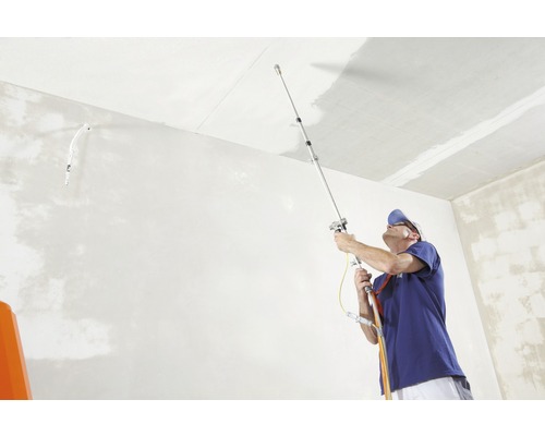 Un homme utilise un pulvérisateur de peinture pour peindre un plafond de pièce.