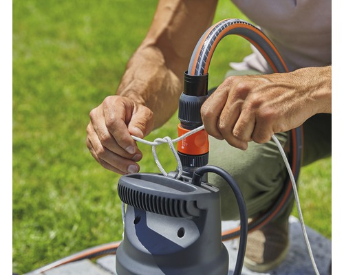 Person befestigt einen Schlauch an einer Gartenpumpe mit Seil