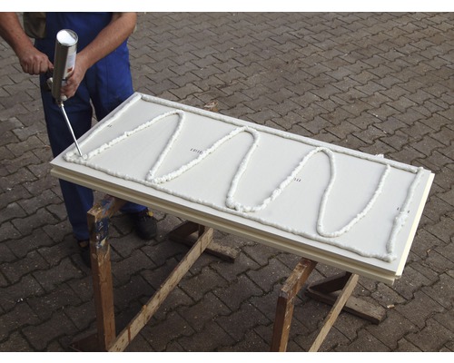 Artisan appliquant de la mousse expansive sur un panneau isolant