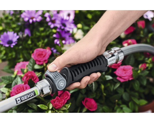 Eine Hand bedient einen GEKA-Wasserschlauch mit Stecker vor Blumen.