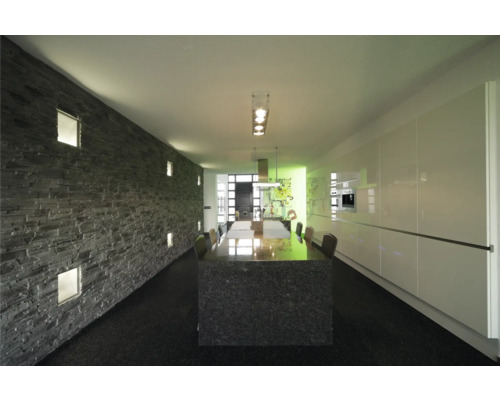 Heller Raum mit Steindekorwand, Esstisch und Küchenzeile.