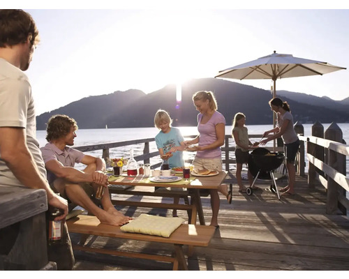 Famille faisant un barbecue sur une jetée en bois au bord d''un lac avec un barbecue, un parasol et une table de pique-nique