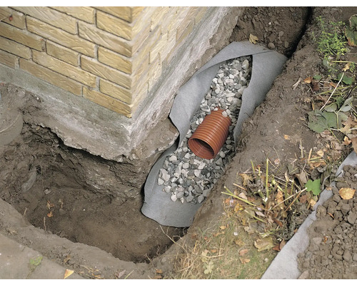 Tranchée de drainage avec tuyau de drainage, gravier et non-tissé de protection à la base d''une maison.