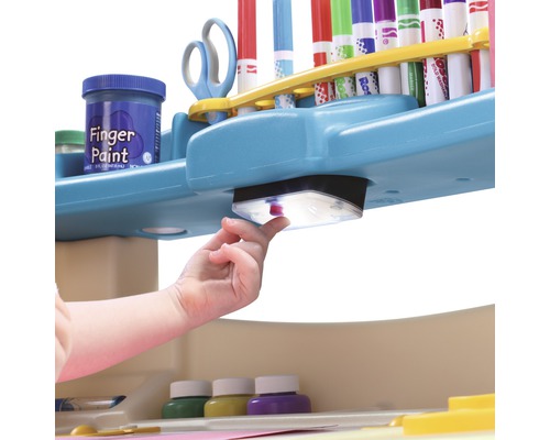 Detailansicht eines Kindertisches mit Fingerfarben, Stiften und einer integrierten Lampe, die von einem Kind bedient wird.