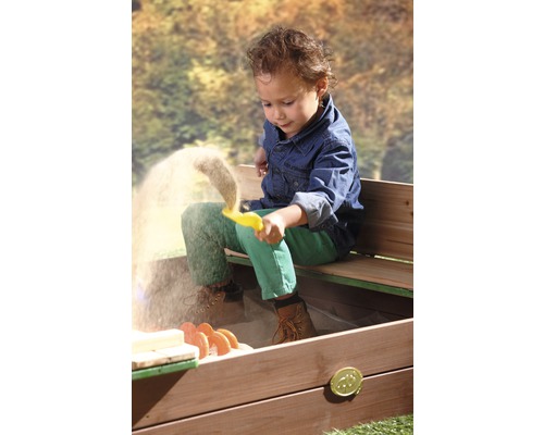 Ein Kind spielt mit einem gelben Förmchen im Sandkasten mit Sitzbank.